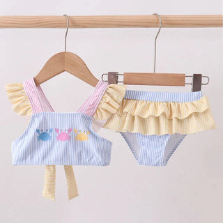 Children's swimsuit set with ruffled top and striped bottom on hangers against a light background