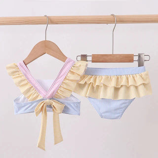 Pastel-colored ruffled swimsuit hanging on a wooden rack against a white background.