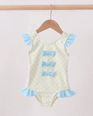 Swimsuit with seashell pattern and blue bows on a hanger against a light background
