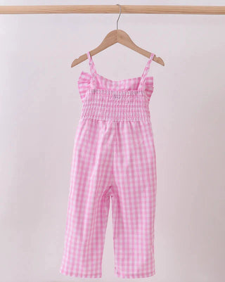 Pink checkered jumpsuit hanging on a wooden hanger against a light pink background