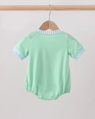 Green baby romper with blue trim on a wooden hanger against a light gray background