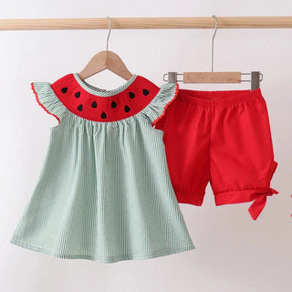 Children's outfit with watermelon-themed top and red shorts on hangers against a white background