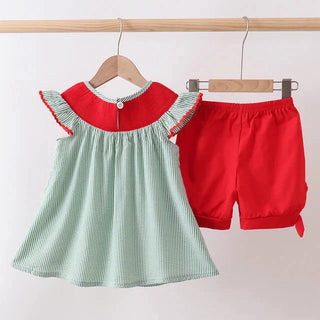 Children's outfit with green top and red shorts on hangers against a white background