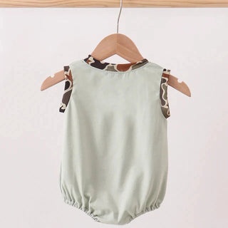 Light green baby romper with brown and beige patterned straps on a wooden hanger against a white background