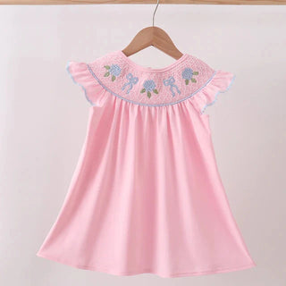 Pink dress with embroidered details on a wooden hanger against a light background