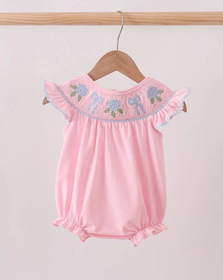 Pink baby romper with floral embroidery on a wooden hanger against a light pink background