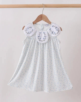 White dress with floral embroidery on a wooden hanger against a beige background