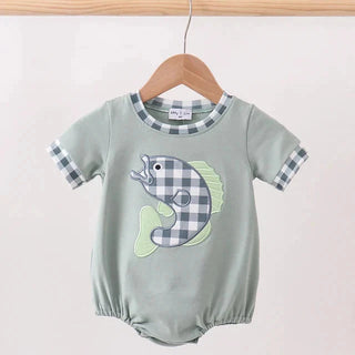Green baby romper with fish design on a wooden hanger against a light pink background