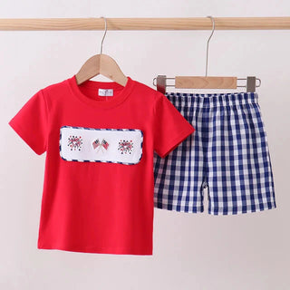 Red t-shirt with white embroidery and blue checkered shorts on a wooden hanger against a white background