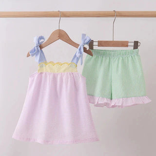Pastel pink top and green shorts on hangers against a white background