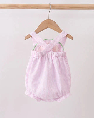 Pink baby romper with criss-cross straps on a wooden hanger against a white background