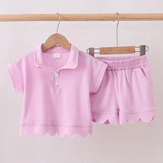 Pink children's outfit with a shirt and shorts on hangers against a light background