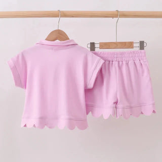 Pink children's outfit with shirt and shorts on hangers against a white background