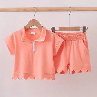 Coral-colored children's outfit with a shirt and shorts on hangers against a light background