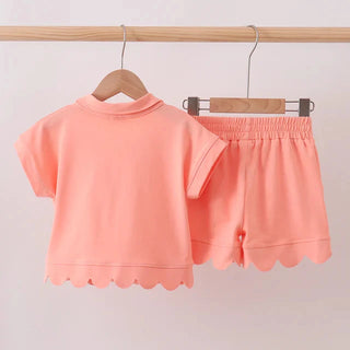 Coral pink outfit with top and shorts on hangers against a light background