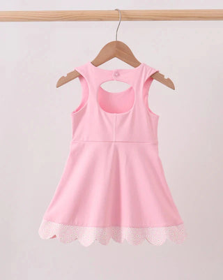 A light pink sleeveless children's dress with a scoop neckline and a scalloped lace hem, hanging on a wooden hanger from a wooden clothes rack against a plain light background.
