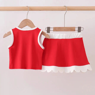 A two-piece children's outfit set consisting of a sleeveless red top with white trim and a matching red skirt with a white scalloped hem, hanging on wooden hangers from a light wood clothing rack against a plain light background.