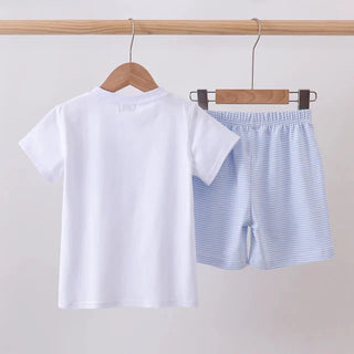 A two-piece kids' clothing set hanging on wooden hangers from a wooden rod. The set includes a white short-sleeve t-shirt and light blue and white striped shorts with an elastic waistband.