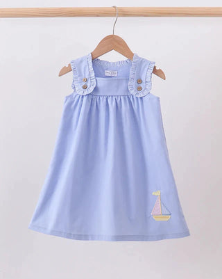 A light blue sleeveless dress with ruffled shoulder straps and a small embroidered sailboat motif near the lower right hem, hanging on a wooden hanger against a plain light background.