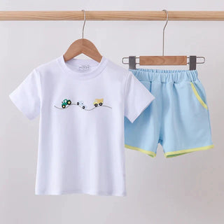 A children's two-piece outfit set featuring a white short-sleeve t-shirt with a small embroidered vehicle graphic on the chest, and light blue shorts with neon yellow-green trim, hanging on wooden hangers against a plain light gray wall.