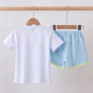 A children's two-piece outfit hanging on wooden hangers from a wooden rod. The set includes a plain white short-sleeve T-shirt and light blue shorts with a thin yellow-green trim at the hem.