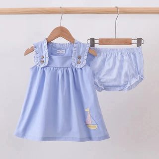 A baby girl's two-piece outfit set consisting of a light blue sleeveless dress with ruffled straps and a small sailboat embroidery, paired with matching light blue and white striped bloomers, hanging on wooden hangers against a plain light gray wall.