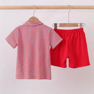 A children's two-piece clothing set hanging on a wooden rod, featuring a short-sleeve polo shirt with thin red and white horizontal stripes and solid red shorts.
