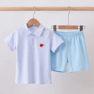 A children's two-piece outfit set hanging on a wooden rod, featuring a white short-sleeve polo shirt with thin blue horizontal stripes and a small red embroidered apple on the chest, paired with light blue shorts.