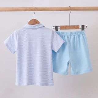 A two-piece children's outfit set consisting of a light blue and white striped short-sleeve polo shirt and light blue shorts, hanging on wooden hangers from a wooden clothing rack against a plain light background.
