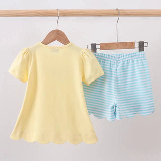 A children's two-piece outfit hanging on wooden hangers against a plain light background. The set includes a pale yellow short-sleeve top and light blue horizontally striped shorts.