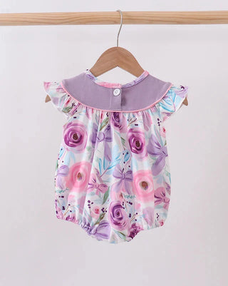 A baby romper with a purple floral print and a lavender collar, hanging on a wooden hanger against a plain white background.