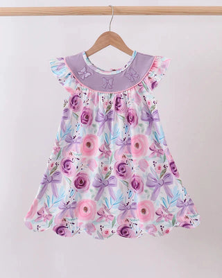 A toddler girl's sleeveless dress with a purple floral print, hanging on a wooden hanger against a plain light background.