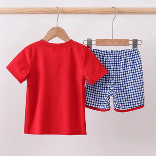A two-piece children's outfit hanging on wooden hangers from a light wood rod. The set includes a solid bright red short-sleeve t-shirt and blue-and-white gingham patterned shorts with a red hem.