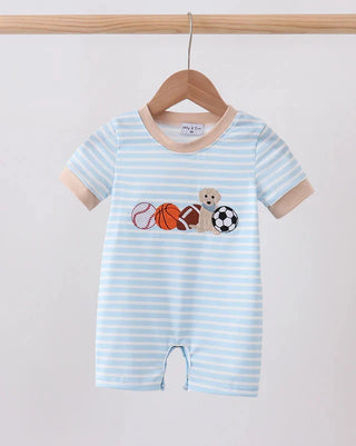 A baby short-sleeve romper with light blue and white horizontal stripes, featuring a colorful sports-themed graphic on the chest with a puppy, basketball, soccer ball, and tennis racket. The romper is displayed on a wooden hanger hanging from a wooden rod against a plain light background.