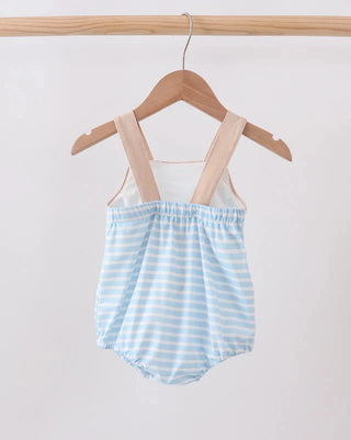 A baby romper with light blue and white horizontal stripes, featuring beige shoulder straps, hanging on a wooden hanger from a wooden clothes rack against a plain white background.