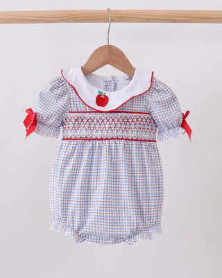 A baby girl's short-sleeve bubble romper hanging on a wooden hanger. The romper features a white collar with red trim, a red apple applique at the center chest, and red and blue smocked horizontal stripes across the bodice.