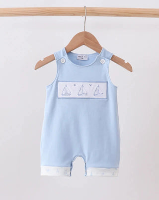 A light blue baby romper with a white sailboat graphic on the chest, hanging on a wooden hanger from a wooden clothes rack against a plain white background.