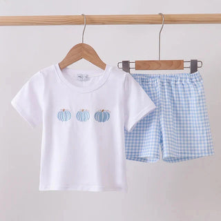 A children's two-piece outfit set hanging on a wooden rod, featuring a white short-sleeve T-shirt with three small blue and orange pumpkin graphics on the chest, and light blue and white gingham check shorts.