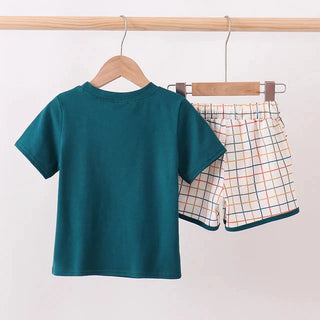 A children's two-piece clothing set hanging on wooden hangers from a light wood rod. The set includes a solid teal green short-sleeve t-shirt and matching plaid shorts in beige, white, and green.