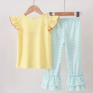A toddler girl's two-piece clothing set hanging on wooden hangers from a wooden rod. The set includes a pale yellow short-sleeve top with ruffled edges and light blue and white striped ruffled flare pants.