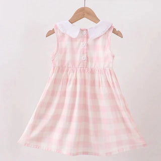 A sleeveless pink and white gingham dress for a toddler girl, featuring a white Peter Pan collar and three front buttons, hanging on a wooden hanger against a light beige wall.