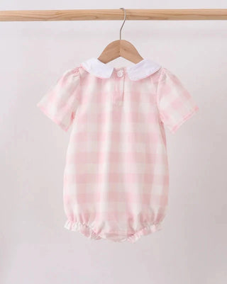 A baby short-sleeve romper in a light pink and white gingham check pattern, featuring a white Peter Pan collar and a buttoned neckline, hanging on a wooden hanger from a wooden clothes rack.