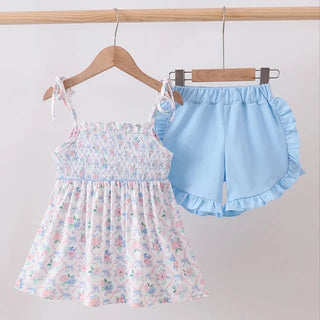 A toddler girl's two-piece clothing set hanging on wooden hangers against a plain light background. The set includes a sleeveless smocked bodice top with a pastel floral print and matching ruffled shorts in light blue.