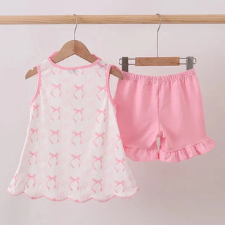 A two-piece children's outfit set hanging on wooden hangers against a plain light background. The set includes a white sleeveless top with pink trim and a repeating pink bow print, paired with pink shorts featuring a ruffled hem.