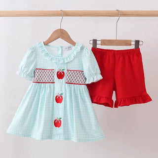 Children's outfit with checkered top and red shorts on hangers against a white background