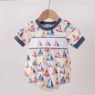 A baby short-sleeve romper with a colorful sailboat print, hanging on a wooden hanger from a light wood rack against a plain off-white wall.