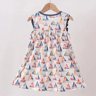 A sleeveless tiered dress for a toddler girl, featuring an all-over sailboat print on an off-white background. The dress is hanging from a wooden hanger on a light wood clothing rack against a plain white wall.