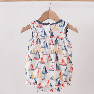 A sleeveless baby romper with an all-over sailboat print, hanging on a wooden hanger from a wooden clothes rack against a plain light background.