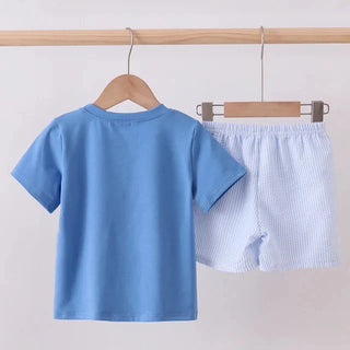 A two-piece children's outfit set consisting of a solid light blue short-sleeve t-shirt and light blue and white vertically striped shorts, displayed on wooden hangers hanging from a wooden clothing rack.