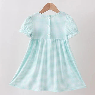 A light mint green and white gingham dress with short puff sleeves and a buttoned back, hanging on a wooden hanger from a wooden clothes rack against a plain light background.